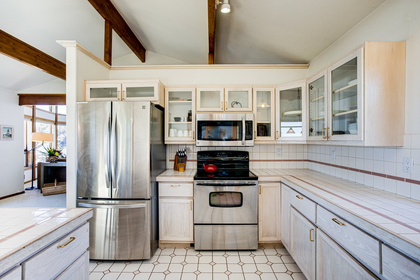 Stainless steel kitchen appliances with tile counter-tops in a sunlit kitchen.