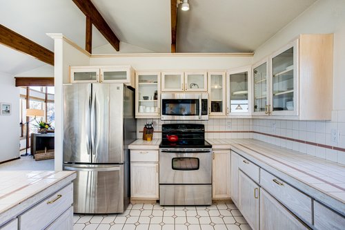 Stainless steel kitchen appliances with tile counter-tops in a sunlit kitchen.